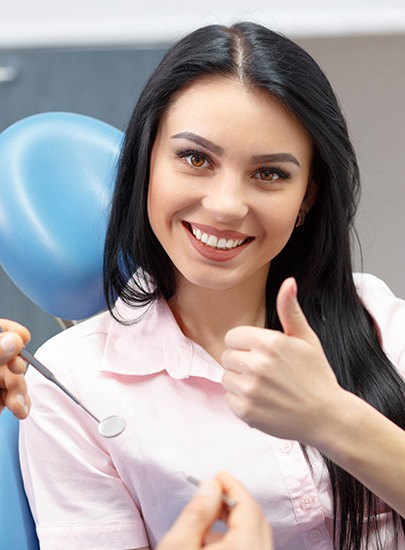 Woman giving thumbs up during dental checkup to prevent dental emergencies
