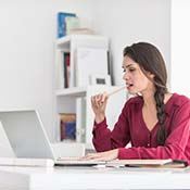 woman sitting at a desk and chewing on a pencil 