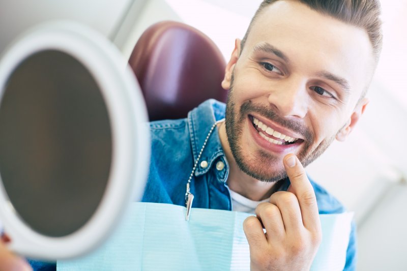 Patient smiling while looking at reflection in dentist's mirror