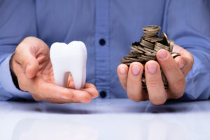 Man's Hand Holding White Tooth And Golden Coins Over Desk