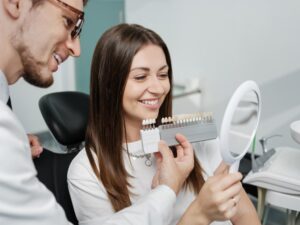 Young woman smiling at dentist's office looking at veneer models.