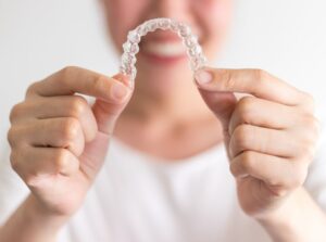 Person holding clear aligner in close-up in foreground.